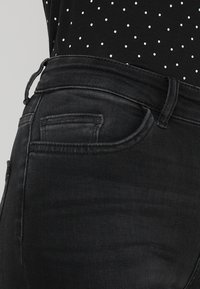 Black denim jeans featuring a standard five-pocket design, slightly faded texture, and a belt loop at the waist.