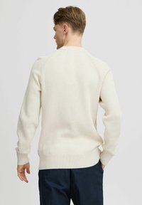 Maglione a coste di colore crema con scollatura rotonda e maniche lunghe, caratterizzato da un orlo aderente e cuciture a raglan. Tessuto morbido e materiale leggero.