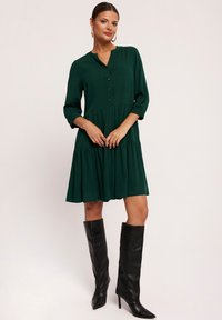 Zielona sukienka do kolan z guzikami z przodu, rękawami o długości trzech ćwierć oraz falbanami. Połączona z czarnymi, wysokimi botkami.