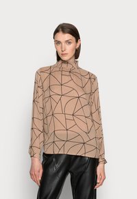 Beige Bluse mit langen Ärmeln und abstraktem schwarzem geometrischem Muster, hohem Kragen mit Rüschensaum, kombiniert mit schwarzen Lederhosen.