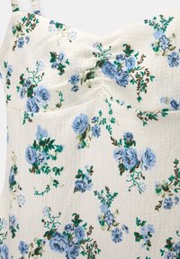 Robe en tissu texturé blanc avec un décolleté cœur et un motif floral bleu présentant des feuilles vertes et des tiges brunes.