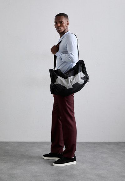 SAC DE VOYAGE NOIR ET GRIS AVEC UNE FORME SOUPLE, DOTÉ D'UN MOTIF ABSTRAIT PROMINENT. TISSU DOUX AVEC DEUX ANSES ET UNE SANGLE DE PORTE. 