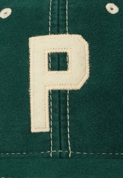 Casquette en tissu vert ornée d'une grande lettre "P" en feutre blanc cousue sur le devant. Coutures blanches visibles le long des coutures.
