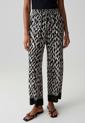Pantalon ample à motif ondulé noir et blanc avec taille élastiquée à cordon, associé à des sandales noires et un haut noir, porté par une personne debout.