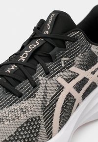 Textilsportschuh mit schwarzem und grauem gewebtem Obermaterial, pinken Akzenten an den Schnürsenkeln und dem Logo sowie einer weißen gepolsterten Sohle.