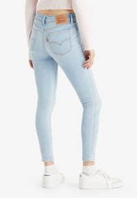 Jeans skinny bleu clair au design classique, avec une patch en cuir à l'arrière de la taille et deux poches arrière. Portés avec des baskets blanches.