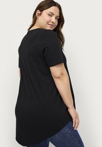 Zwarte T-shirt met korte mouwen, een ronde halslijn en een gebogen zoom. Zachte stof met een losse pasvorm, voorzien van een subtiele naad aan de achterkant.