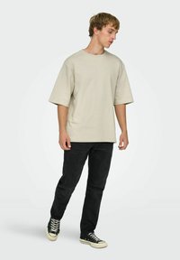 Beige oversized t-shirt med korte ærmer, kombineret med sorte jeans og sorte sneakers. Simpelt design, blød tekstur og afslappet pasform.