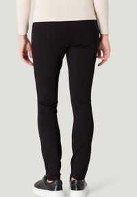 Leggings noirs en tissu doux et extensible. Ils présentent une coupe ajustée, une texture lisse et sont associés à des baskets noires à semelles blanches.