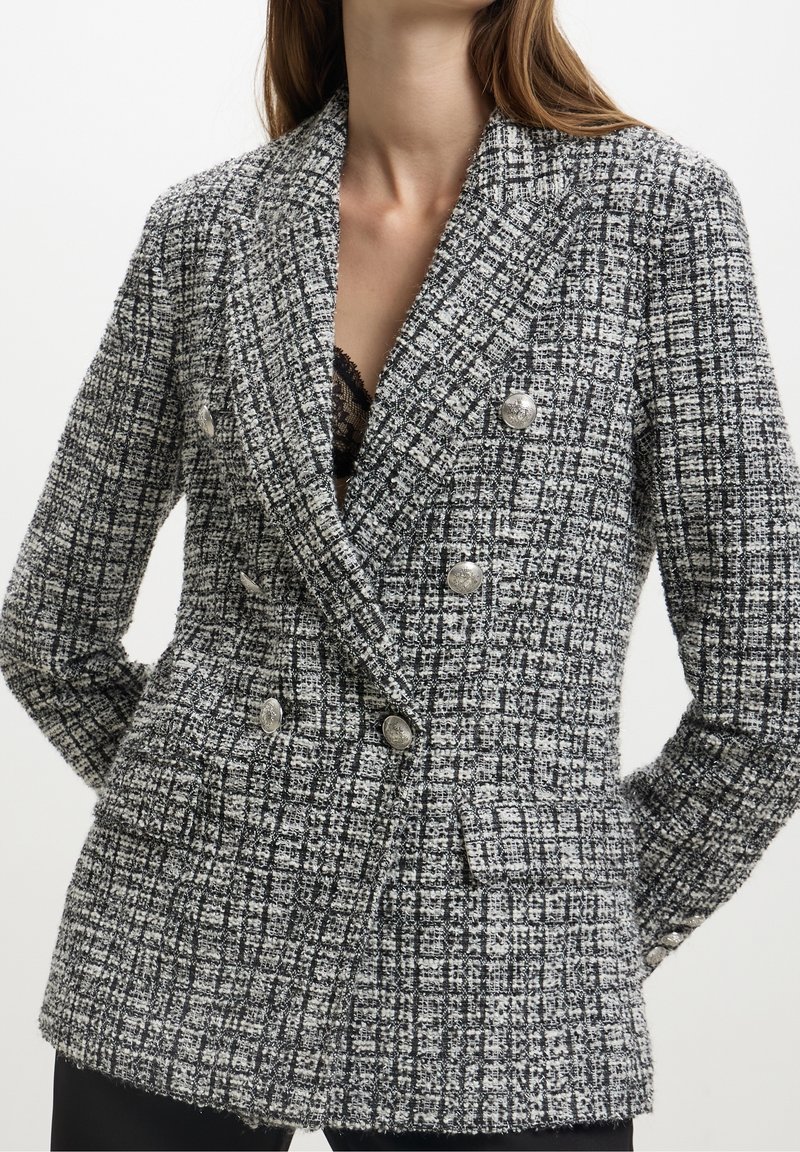 Blazer bicolore nero e bianco a doppio petto con dettagli in bottone argentato, rever a notche e due tasche frontali.
