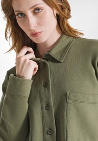 Olijf groen button-up shirtjacket in een gemêleerde stof, met een kraag, een voorzak en vijf knopen. Eenvoudig ontwerp en een relaxte pasvorm.