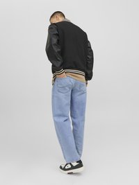 Veste de varsity noire avec manches en cuir, col à rayures, chemise beige en dessous, jeans bleu clair et baskets noires avec accents blancs.