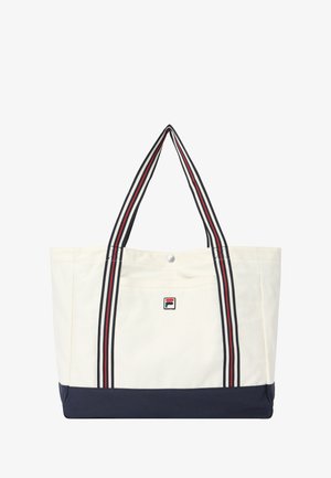 Valkoinen ja tummansininen olkalaukku, jossa on raidalliset kahvat ja pieni suorakaiteen muotoinen logo etutaskussa, joka on suljettu hopeisella napilla.