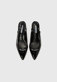 Čierne lodičky na podpätku so zadným popruhom z lakovanej kože s špicatou špičkou, s logom na prednej časti a päte. Hladká textúra, minimalizované dizajnové prvky.
