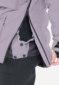 Lyserød isoleret jakke med lynlås foran, indre foer og trykknaplukninger. Har sorte detaljer og elastiske manchetter.
