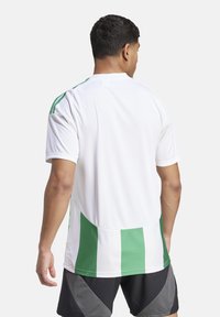 Weißes Sportshirt mit grünen vertikalen Streifen, ausgestattet mit einem Rundhalsausschnitt und kurzen Ärmeln. Das Material wirkt leicht und atmungsaktiv.