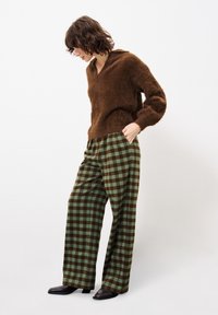 Brauner, flauschiger Kapuzenpullover kombiniert mit weit geschnittenen, grün-braun karierten Hosen. Schwarze Stiefeletten runden das Outfit ab.