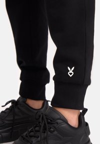 Melni sporta bikses ar ribotām piedurknēm, ar baltu sirds un zaķa logotipu apakšstilbā. Apvienotas ar melniem sporta apaviem.