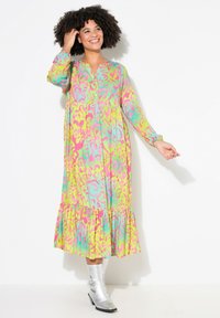 Vestito colorato con lunghezza al ginocchio, scollatura a V, maniche lunghe, motivo astratto nei colori rosa, verde e turchese, e orlo a volant. Stivali argentati.