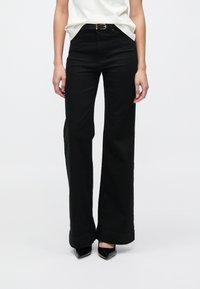 Μαύρο παντελόνι με φαρδύ πόδι και ψηλή μέση, κατασκευασμένο από συμπαγές βαμβάκι. Διαθέτει θηλιές για ζώνη και μανσέτες στο τελείωμα. Ομαλή υφή και ραμμένο σχέδιο.