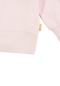 Helles rosa Sweatshirt mit geripptem Saum, ausgestattet mit einem kleinen gelben Etikett. Glatte Textur mit lässiger Passform, keine sichtbaren Muster.
