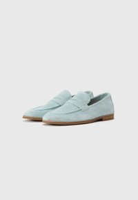 Mocasines de ante azul claro con textura perforada, suela plana y una correa cosida en el empeine. Punta redondeada y diseño minimalista.