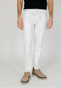 Pantalones de mezclilla blanca con un corte ajustado, cinco bolsillos y una textura sutilmente desgastada. Combinados con zapatos beige de cordones con suelas de goma.