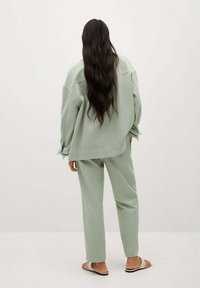 Světle zelená sada domácího oblečení obsahující přes oversized, volný top a zúžené kalhoty, vyrobená z měkké látky s hladkým povrchem.