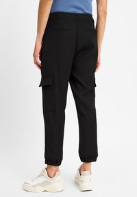 Schwarze Cargo-Hosen mit elastischen Bündchen, ausgestattet mit seitlichen Taschenklappen und Gesäßtaschen, gefertigt aus einem glatten, leichten Stoff.