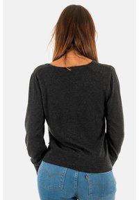 Dunkelgrauer Pullover mit weitem Ausschnitt und langen Ärmeln, aus weichem Stoff. Kombiniert mit blauen Jeans, die einen gerippten Saum zeigen.