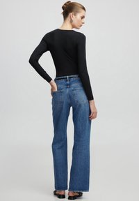 Zwarte langslavige bodysuit gecombineerd met hooggewaaid blauwe denim jeans. De jeans hebben een rechte pijp en vier zakken.