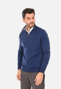 Maglione zip-up blu navy con colletto alto, polsini e orlo a costine. Realizzato in un tessuto testurizzato. Presenta un colletto interno a contrasto.