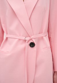Rozā pielāgota blazera ar iedragāmu apkakli, jostu viduklī un melnu pogu detaļu. Gluda tekstūra ar divām priekšējām kabatām.