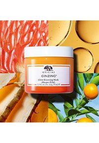 Crème gel orange dans un pot transparent avec un couvercle blanc. L'étiquette présente un texte noir sur fond blanc. Autour, des motifs de fruits vibrants et de textures.
