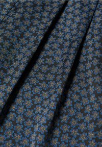 Schwarzer Stoff mit einem sich wiederholenden Muster aus kleinen blauen, lila und gelben Blumenformen, dargestellt mit sanften Falten.