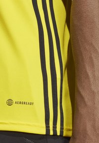 Geel sportshirt met zwarte zijkanten, gemaakt van soepel materiaal, met een "AEROREADY" logo aan de zoom.