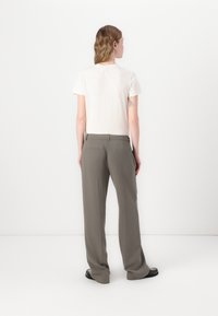 Lys beige t-shirt med korte ærmer parret med løse, grå bukser med en talje og to baglommer, vist fra bagenden.