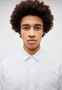 Καρό πουκάμισο σε ανοιχτό μπλέ με λευκές ρίγες, βαμβακερό ύφασμα, μυτερός γιακάς, μία τσέπη στο στήθος και λεπτομέρεια με κεντητό λογότυπο.