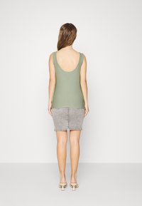 Top sem mangas verde-azeitona com um decote profundo nas costas, combinado com uma saia-lápis de denim cinza. Modelo usa sandálias de salto bloco bege.