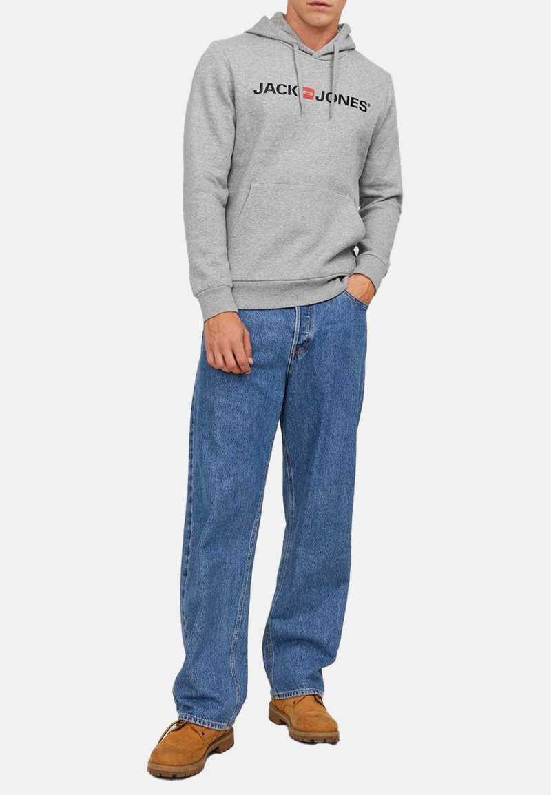 Grå sweatshirt med logo, forlommer og snøre-hætte, kombineret med løse blå jeans og brune sko.