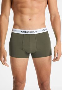 Boxer aderenti verde oliva con una cintura bianca "GUESS JEANS". Realizzati in un tessuto liscio e elastico con un design della sacca sagomata.