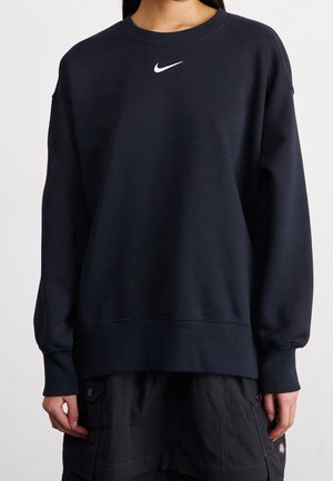 Personne portant un sweat-shirt bleu marine uni avec un petit logo Nike blanc centré près du col et un pantalon cargo foncé.
