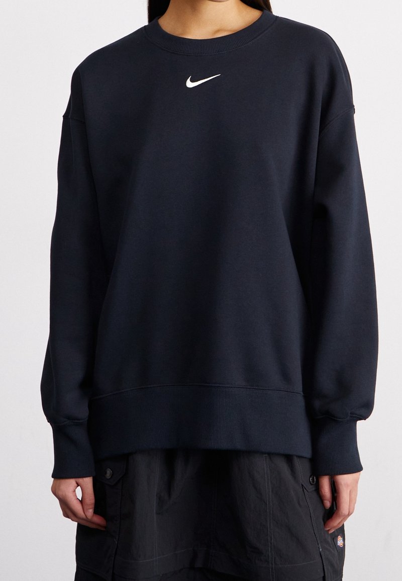 Personne portant un sweat-shirt bleu marine uni avec un petit logo Nike blanc centré près du col et un pantalon cargo foncé.