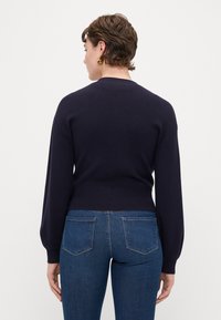 Ναυτικό πλεκτό πουλόβερ με μπαλόνι μανίκια και ριμπ αφαίρεση. Συνδυασμένο με εφαρμοσμένα μπλε τζιν, δείχνοντας πίσω όψη και απλά σχεδιαστικά στοιχεία.