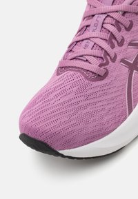 Světlofialová sportovní obuv s horní částí z síťoviny, texturovaným povrchem a zesílenou špičkou; má ploché tkaničky a černou gumovou podrážku.