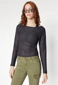 Svart långärmad topp med texturerad tyg och rund halsringning, kombinerad med olivgröna cargobyxor med fickor och en figursydd silhuett.