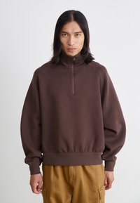 Brun kvartdragningströja med avslappnad passform, raglanärmar, ribbade ärmslut och en något samlad nederkant. Slät textur och mjukt tyg.