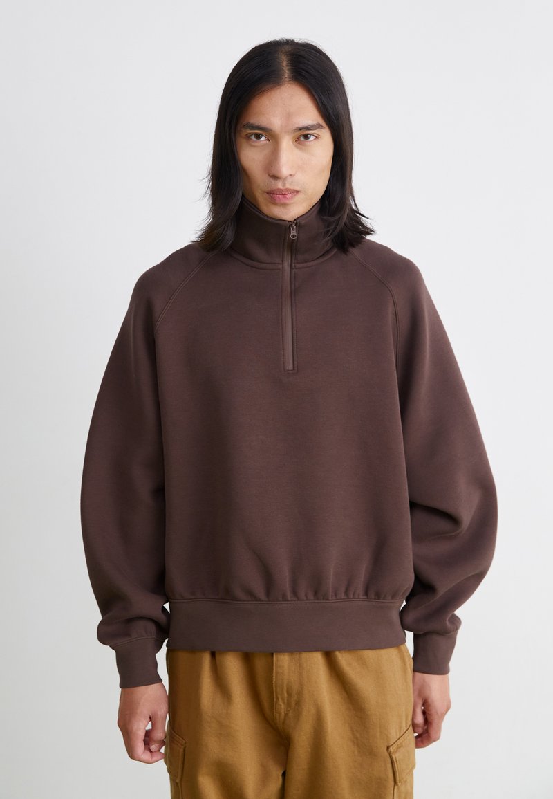 Brun kvartdragningströja med avslappnad passform, raglanärmar, ribbade ärmslut och en något samlad nederkant. Slät textur och mjukt tyg.