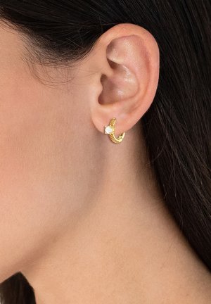 Goldene Creole mit strukturiertem Design, einem kleinen Perlenakzent und einer offenen kreisförmigen Form, getragen am Ohrläppchen.