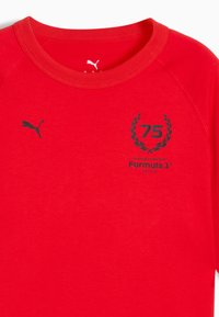 Rød bomulds T-shirt med rund halsudskæring, korte raglanærmer og sort trykte grafikker: "75," en laurbærkrans, og "Formula 1."